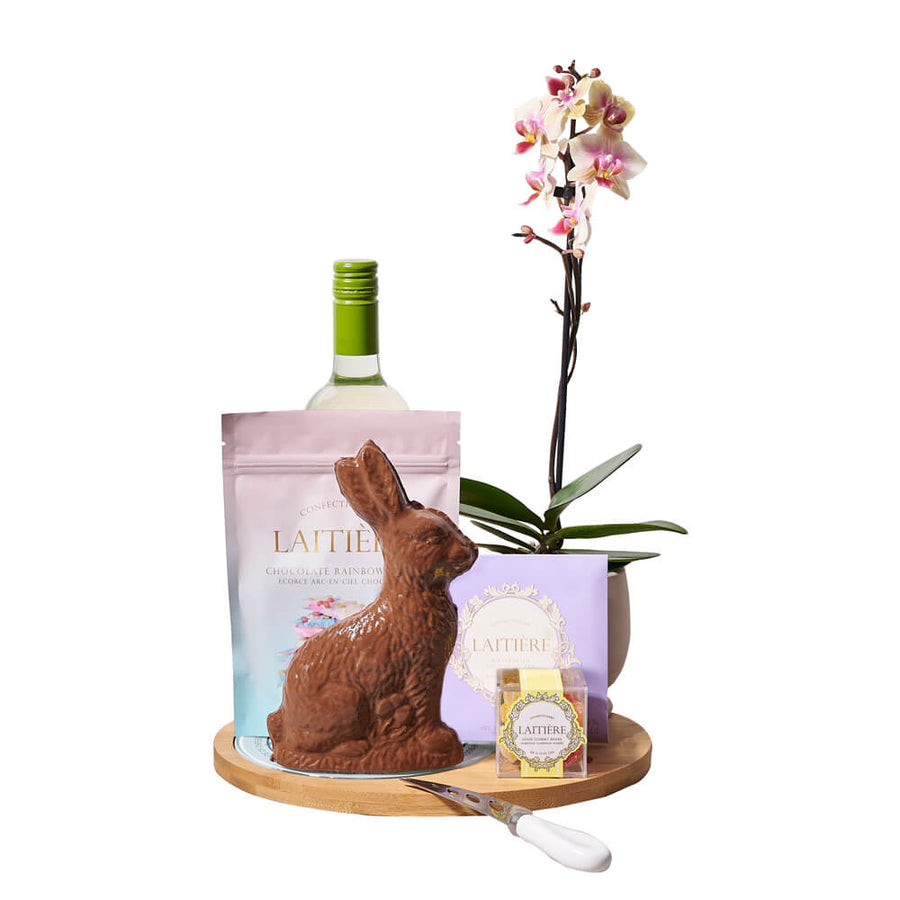 Orchid & Wine Easter Gift, milk chocolate bunny, rainbow chocolate bark, a bar of chocolate, sour gummy bears, a bottle of wine, a beautiful potted orchid plant, and a wood & glass serving board, Easter Gifts from Blooms Canada - Same Day Canada Delivery.